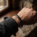 CAIRN matte hematite bracelet worn on a man's wrist by a window