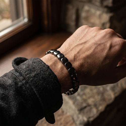 CAIRN matte hematite bracelet worn on a man's wrist by a window
